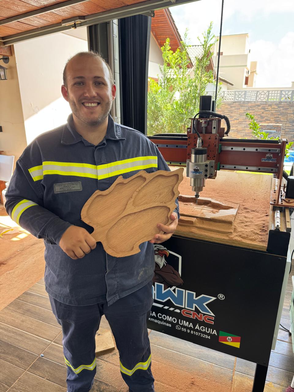 Cliente sorrindo com peça de madeira ao lado da CNC Hawk